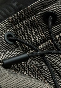 Gros plan sur un tissu pied-de-poule noir et beige avec un cordon noir passant à travers deux œillets métalliques noirs.