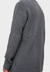 Grauer Strickpullover mit geripptem Muster, langen Ärmeln und lockerem Schnitt, mit einem kleinen Logoetikett an der unteren Seite.