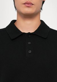 Cămașă polo tricotată neagră, cu guler clasic, sistem de închidere cu trei nasturi și material texturat.
