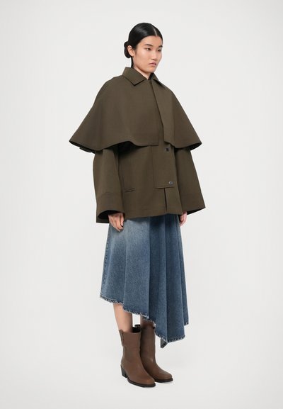 Green wool blend jacket with a cape design, paired with a light blue denim skirt, and brown ankle boots featuring a block heel.