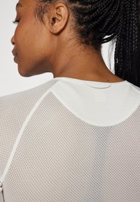 Weißes Mesh-Sportoberteil mit Rundhalsausschnitt, strukturiertem Muster und Kontrastnähten. Die Rückansicht betont das atmungsaktive Material.