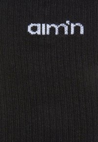 Sorte strikkede sokker med ribbet tekstur og hvid "aimin" logo broderi nær toppen.