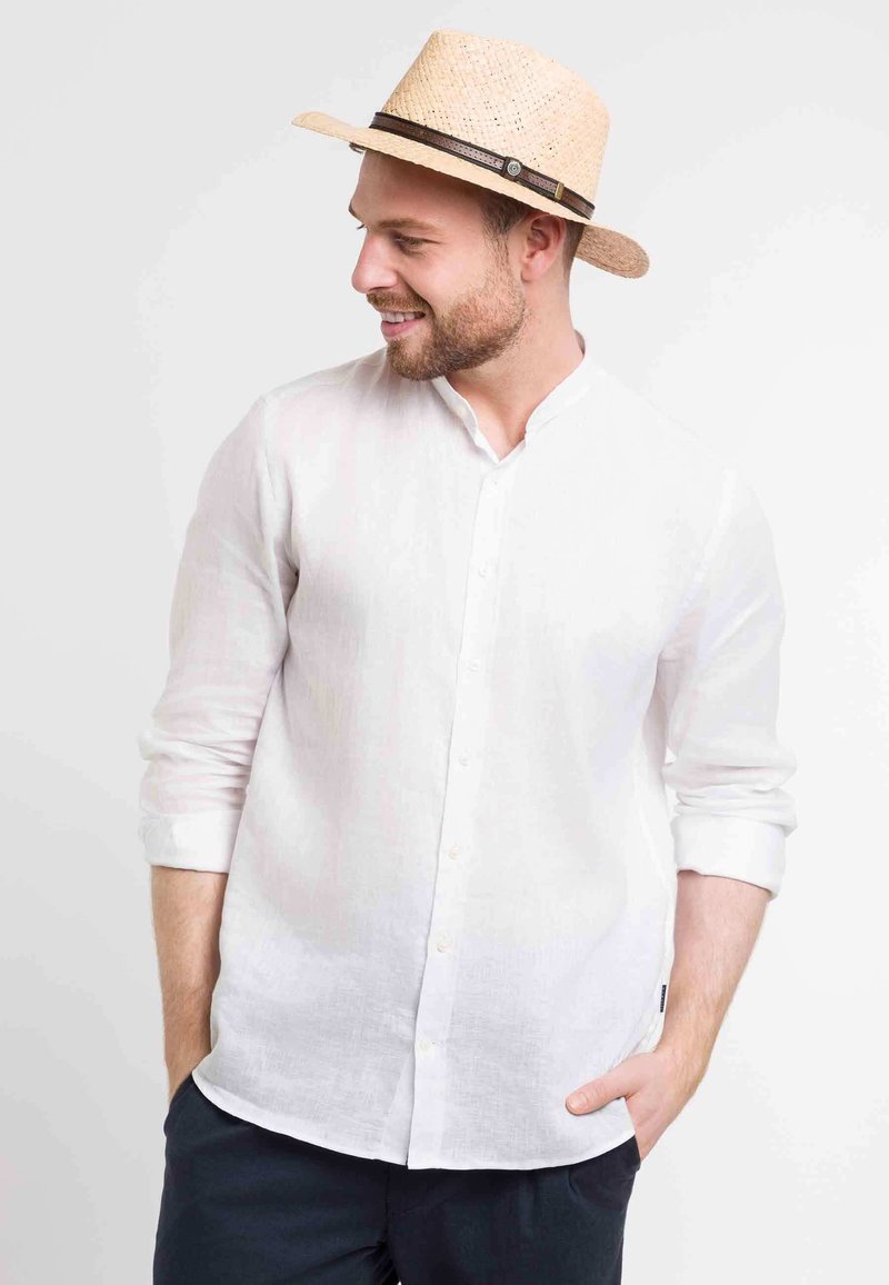 Camisa de lino blanca con cuello mao, mangas largas y detalles de botón, combinada con un sombrero de paja que tiene una banda de cuero marrón.