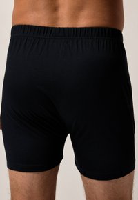 Boxers noirs en coton avec une ceinture élastique, offrant une texture douce et un ajustement confortable. Design simple sans motifs ni accents.