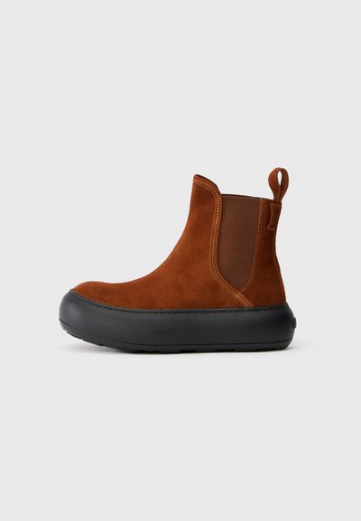 Botine din suede maro, cu panouri elastice laterale, talpă din cauciuc negru, vârf rotund și bandă de prindere la spate pentru a fi ușor de încălțat.