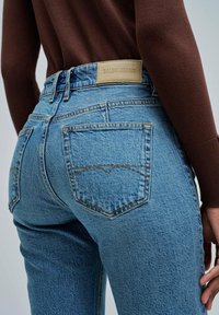 Jeans de mezclilla en un tono azul claro con bolsillos traseros, costuras decorativas y una etiqueta de cuero beige que dice "SALSA JEANS" en la cintura.