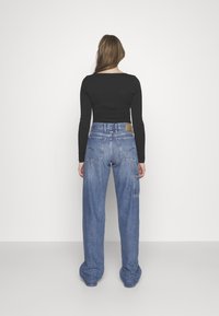 Ljusblå denim vid leggings med hög midja, med bakfickor och ett märke på baksidan, kombinerat med en åtsittande svart långärmad tröja.