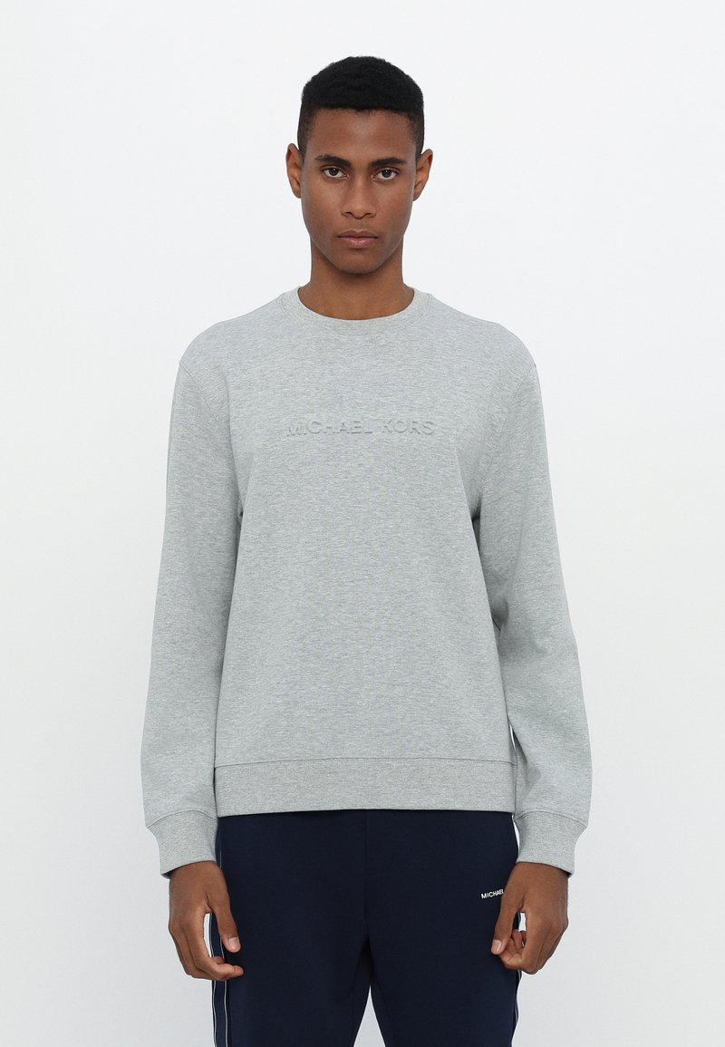 Sudadera gris con cuello redondo, que presenta un logotipo en relieve "MICHAEL KORS" en la parte frontal. Fabricada con un tejido suave y con puños y dobladillo de canalé.
