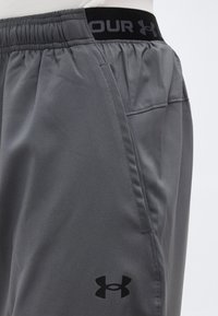 Γκρι αθλητικές βερμούδες με ελαστική μέση που φέρει το λογότυπο Under Armour στη μέση και στο κάτω μέρος του ποδιού.