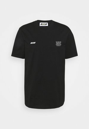 Musta lyhythihainen T-paita, jossa valkoinen "MSGM"-logo vasemmalla rinnalla ja pieni valkoinen teksti oikealla rinnalla, joka kertoo brändin ja koordinaatit.