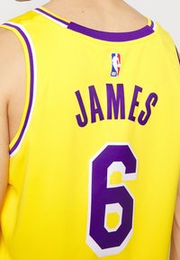 Žlutý basketbalový dres s fialovými akcenty. Na dresu je nápis "JAMES" tučným fialovým písmem a číslo "6" ve velkém, výrazném blokovém stylu.