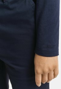 Marineblauwe longsleeve shirt met een gladde textuur, voorzien van gestikte manchetten en de reliëf merknaam "GANT" op de mouw.