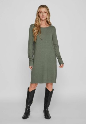 Groene gebreide jurk met lange mouwen, ronde hals en geribbelde zoom. Gecombineerd met hoge zwarte leren laarzen. Gladde textuur, casual ontwerp.
