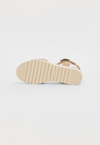 Sandal beige avec une sangle tressée, dotée d'une semelle en caoutchouc texturé avec des stries pour une meilleure adhérence et d'un fond de chaussure lisse. Accentuée par un détail en nœud.