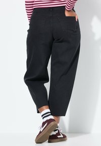 Pantalones de mezclilla anchos y negros con cintura alta y dos bolsillos traseros. Combinados con calcetines a rayas blancas y negras y zapatillas burdeos.