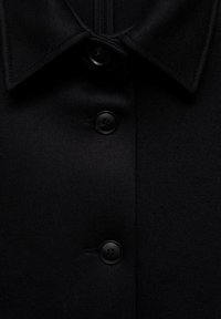 Czarny płaszcz z wyodrębnionym kołnierzem, pięcioma czarnymi guzikami, gładką tkaniną i starannym przeszyciem wzdłuż brzegów.