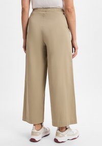 Beige wijde broek met een elastische tailleband, met een gladde textuur en een volle lengte, gecombineerd met lichte witte sneakers.