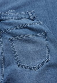 Szczegół tylniej kieszeni niebieskich dżinsów z widocznymi szwami i pętelką na pasek, pokazujący teksturę i splot materiału.