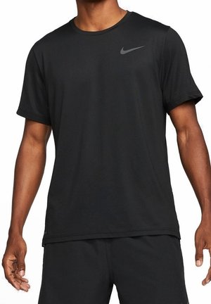 Mężczyzna noszący gładką czarną sportową koszulkę Nike z krótkim rękawem oraz pasujące czarne szorty, stojący z rękami swobodnie opuszczonymi wzdłuż ciała.