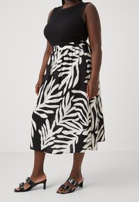 Top sans manches noir associé à une jupe midi à motifs de feuilles noir et blanc. La jupe a une taille élastique et tombe jusqu'au mollet. Sandales à talons noires.