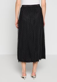 Falda midi negra con lunares y capas de tul, cintura elástica y tejido texturizado. Presenta una silueta fluida y acentos semitransparentes.