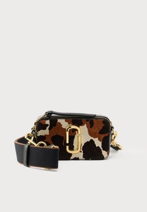 Runderhuid crossbodytas met een koeienprint in bruin en crème, voorzien van gouden accenten, een bovenrits en een afneembare riem.