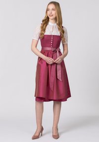 Long pink dress with a fitted bodice, lace sleeves, and a bow at the waist. Button details and a textured underlayer are notable.