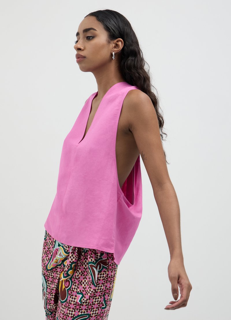 Top sans manches rose avec un décolleté en V profond, présentant de larges emmanchures et une coupe décontractée. Porté avec un pantalon multicolore à motifs.