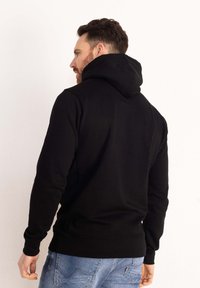 Felpa nera con colletto alto e grande cappuccio, dotata di maniche lunghe e orlo a coste. Tessuto liscio senza motivi o dettagli.