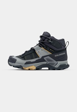Mid-height hiking boot in gray and black with textured upper, lace-up closure, and rubber sole. Features Gore-Tex for waterproofing.
