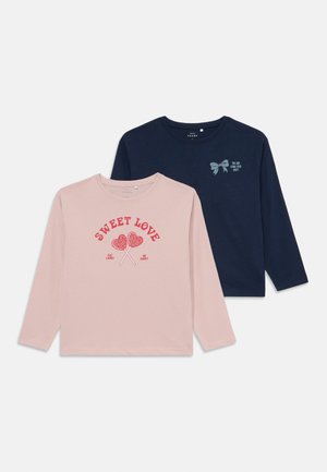 Deux t-shirts à manches longues : l'un rose clair avec un graphisme de sucette et du texte, l'autre bleu marine avec un motif de nœud. Tissu en coton doux.