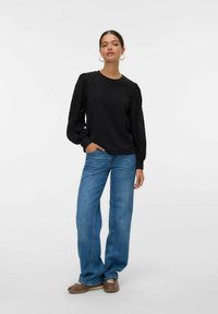 Svart sweatshirt med texturerade puffärmar, matchad med ljusblå vida jeans och bruna skor. Slät tyg med avslappnad passform.