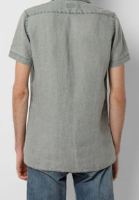 Košile s krátkými rukávy ve světle šedé barvě z lněné tkaniny, s límcem na knoflíky, zadním yoke a zakřiveným lemem. Obsahuje jemnou strukturu a volný střih.