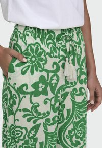 Groene en witte bloemenpatroonbroek met een verstelbare tailleband, zakken en franjes. Lichtgewicht, gestructureerde stof.