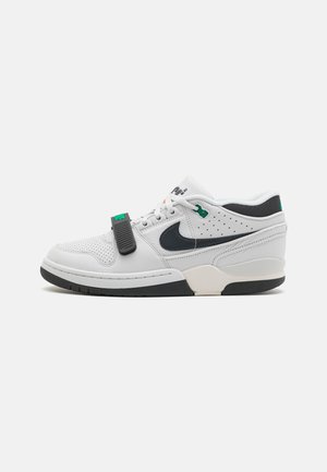 Zapatilla de piel blanca con acentos negros, parte superior texturizada, detalles perforados, correa ajustable, suela de goma y cierre de cordones colorido.