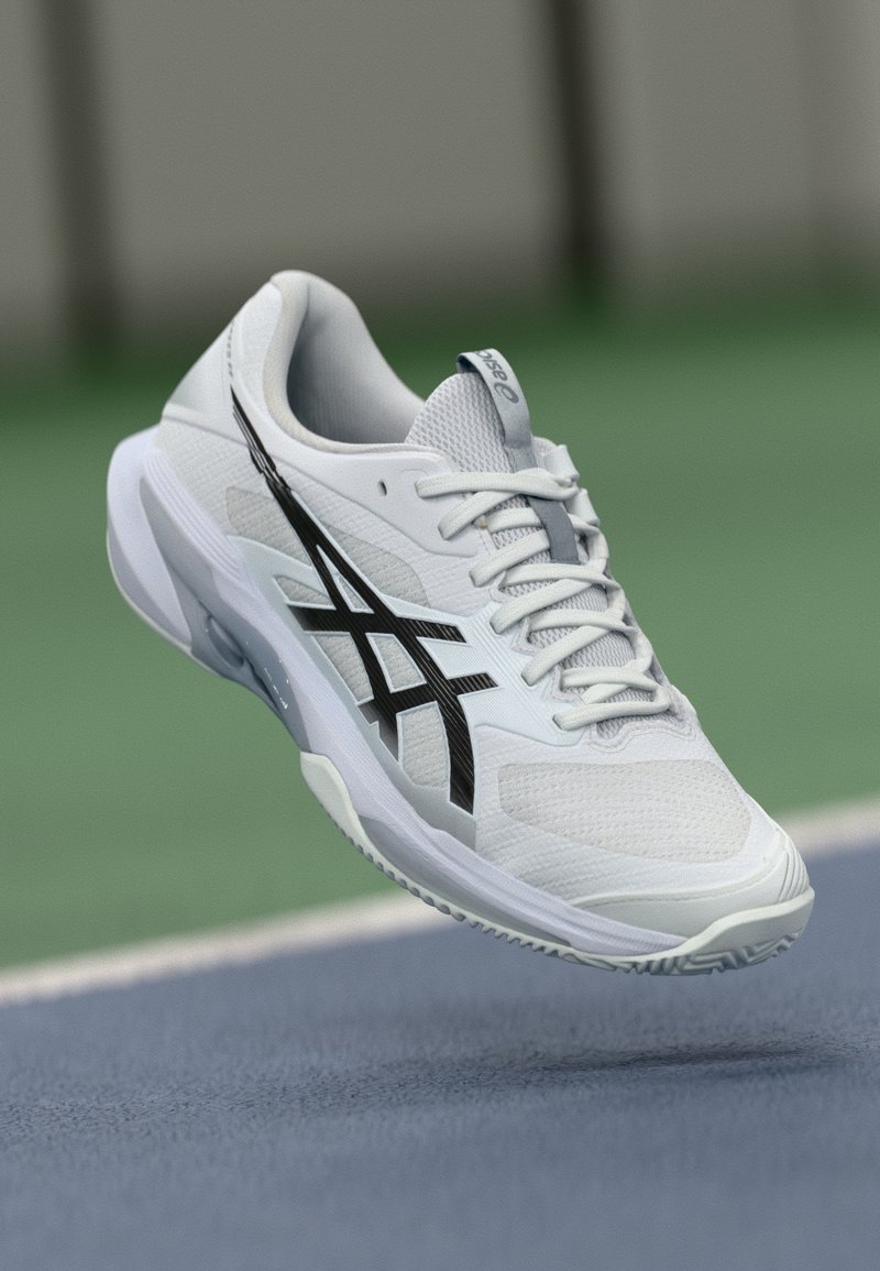 Λευκό αθλητικό παπούτσι με υφασμάτινη επένδυση, μαύρες λεπτομέρειες και ελαστική σόλα, σχεδιασμένο για επιδόσεις. Διαθέτει κορδόνια και λεπτομέρεια λογότυπου.