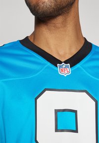 Carolina Panthers futballmez élénk kék színben, fekete V-nyakú gallérral, nagy fehér 9-es számmal és NFL logóval a nyaknál.