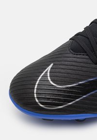 Scarpa da calcio nera con texture rigata, caratterizzata da un grande logo Nike argentato e un accento blu sulla suola. I lacci sono neri.
