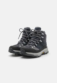 Schwarze und graue Mid-Top-Wanderschuhe mit gemustertem Stoff, dicken grauen Schnürsenkeln und robusten Sohlen für besseren Halt. Vibram-Logo auf der Sohle sichtbar.