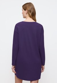 Fioletowa sukienka z długim rękawem, luźny krój, okrągły dekolt i jednolity kolor. Posiada średniej długości krój oraz miękką, gładką teksturę.