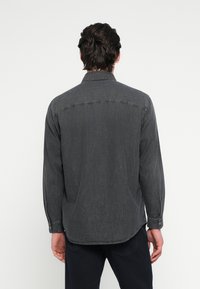 Γκρι μακρυμάνικο πουκάμισο από απαλό ύφασμα με γιακά με κουμπιά, διαθέτει στρογγυλεμένο κάτω μέρος και διακριτικές ραφές.