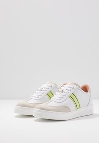 Baskets blanches avec des accents en daim gris et des rayures vert lime, dotées d'un bout rond, d'un système à lacets et d'une semelle en caoutchouc texturée.