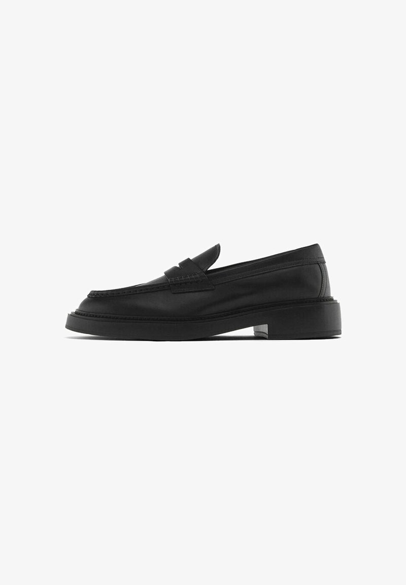 Mocassin en cuir noir avec une semelle plate, bout rond et détails cousus. Présente une simple sangle supérieure. Texture lisse avec des accents minimaux.