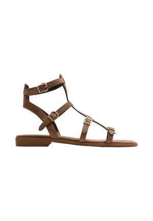 Brun flad gladiatorsandal med fire justerbare spænder i gyldent metal og lukket hæl, vist i profil på hvid baggrund.