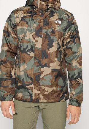 Camouflage-Muster North Face Jacke mit Frontreißverschluss und elastischen Bündchen, getragen zu olivgrünen Hosen.