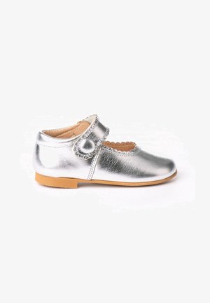 Zapato Mary Jane de cuero plateado con bordes ondulados, acento de botón redondo y suela de goma marrón, que presenta un diseño troquelado en la punta.