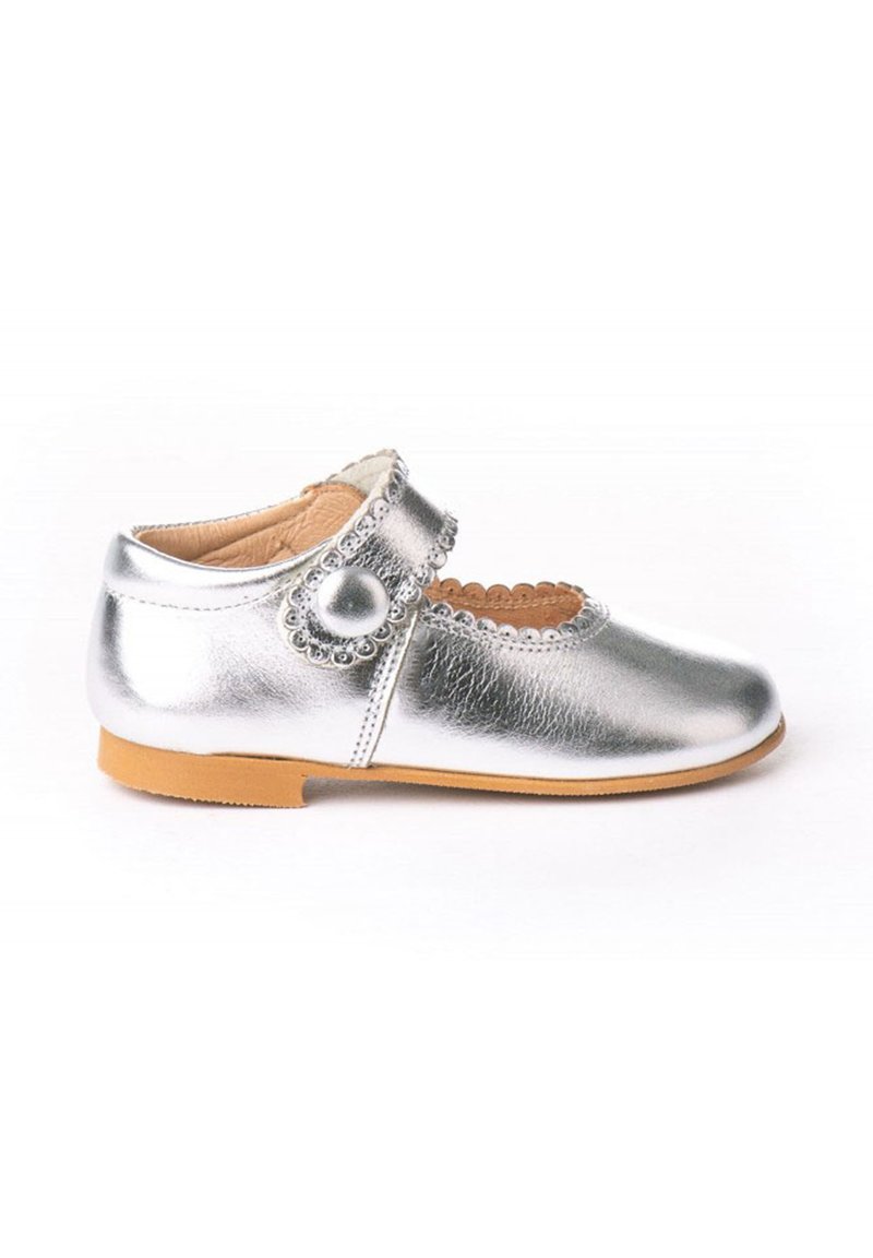 Zapato Mary Jane de cuero plateado con bordes ondulados, acento de botón redondo y suela de goma marrón, que presenta un diseño troquelado en la punta.