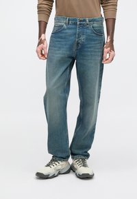 Jasnoniebieskie dżinsy typu denim o luźnym kroju, z pięcioma kieszeniami i delikatnym przetarciem. Połączone z szaro-białymi trampkami.