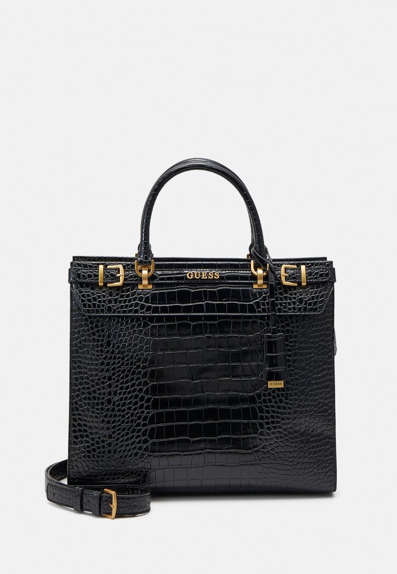 Sac à main noir à texture crocodile, avec poignées supérieures, boucles dorées, bandoulière amovible et logo GUESS sur le devant.