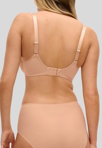 Beige-rintaliivit säädettävillä olkaimilla ja hakaskiinnityksellä. Sileä pinta, jossa hienovarainen aaltoileva reunus. Yhdistetty samansävyisiin beigenvärisiin alushousuihin.